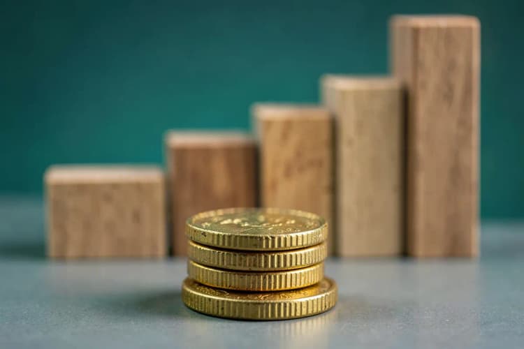 Seção 3: Três moedas de ouro empilhadas em frente a um gráfico de barras ascendente feito de blocos de madeira.